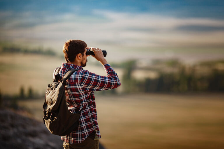 Mies katsoo avarassa maisemassa kiikareilla kohti kaukaisuutta